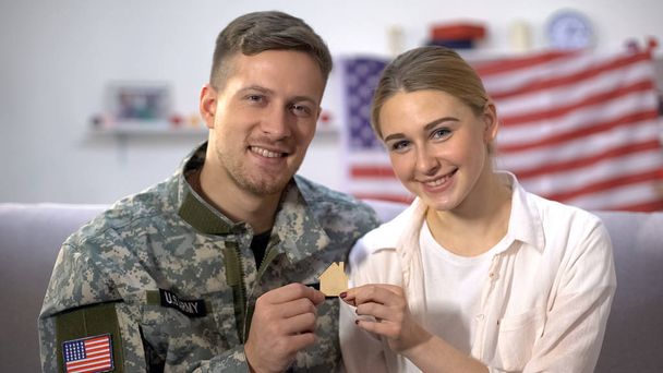 Smiling US male soldier and his wife showing wooden house sign on camera, family - Foto, Imagem