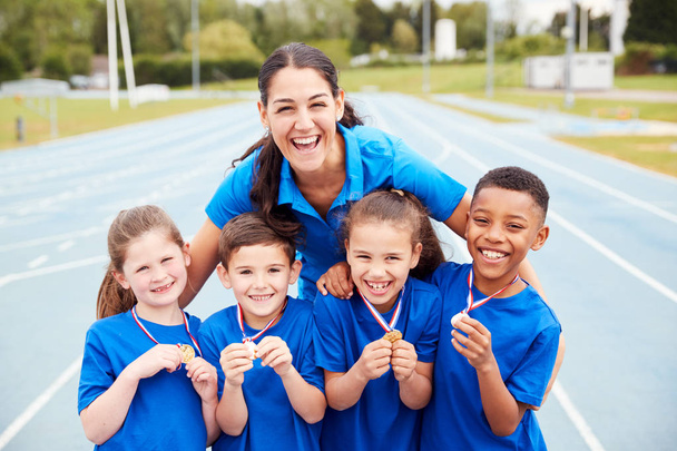 Retrato de niños con entrenador femenino mostrando medallas de ganadores en el día del deporte
 - Foto, imagen