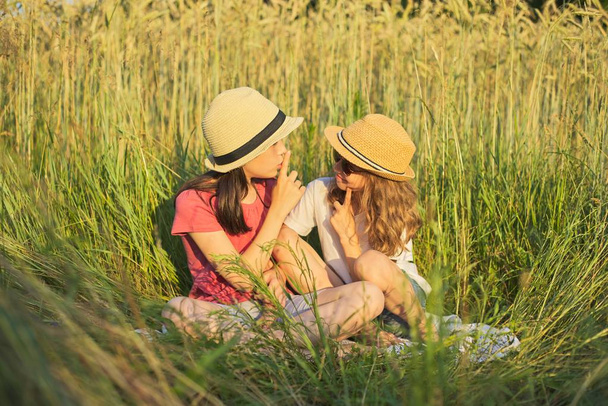 Two smiling girls sitting in grass, children talking - Fotoğraf, Görsel