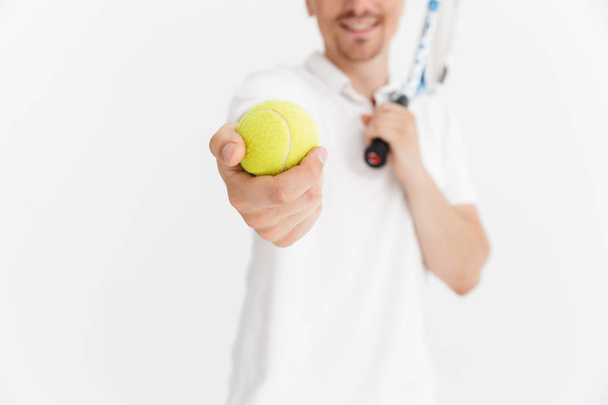 Photo closeup of pleased man in t-shirt holding racquet and ball - 写真・画像