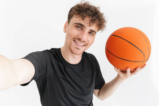 Photo closeup of muscular young man in t-shirt smiling and taking selfie while holding basketball - Foto, Bild