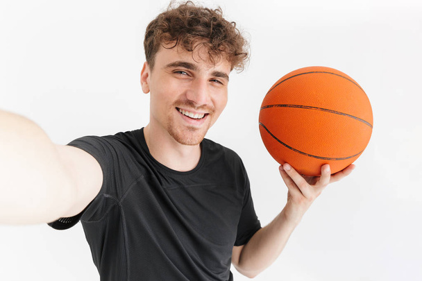 Photo closeup of positive young man in t-shirt smiling and taking selfie while holding basketball - Foto, immagini