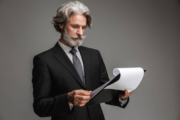 Bild eines erwachsenen kaukasischen Geschäftsmannes im formellen schwarzen Anzug mit Papierdiagrammen - Foto, Bild