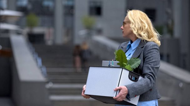 Aged woman with stuff box leaving office building, pension age, work opportunity - Fotografie, Obrázek