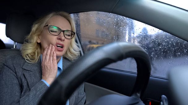 Senior female in business suit feeling toothache driving work car, health care - Φωτογραφία, εικόνα