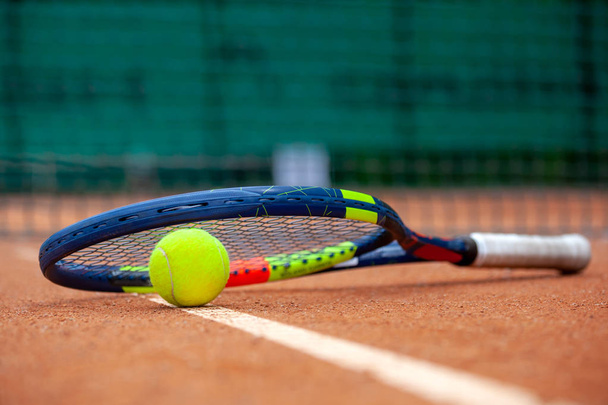 Yellow tennis ball and racket lie on the clay court. - Foto, afbeelding