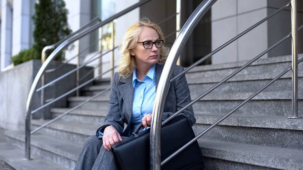 Dismissed senior female accountant sitting stairs looking office, unemployment - Fotografie, Obrázek