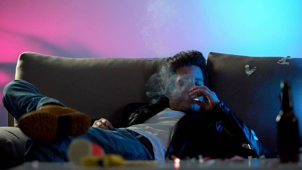 Careless drunk man smoking cigarette and relaxing on sofa at nightclub party - Foto, afbeelding