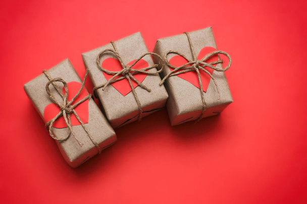 Romantic presents set. Gift boxes wrapped in brown craft paper and tie hemp string. Carton hearts. Red solid background. Delivered parcels.  - Fotografie, Obrázek