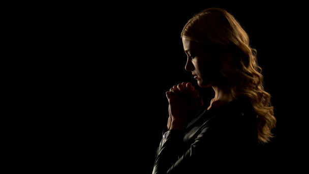 Mulher loira orando em lugar escuro, pedindo perdão, confissão pecadora
 - Foto, Imagem