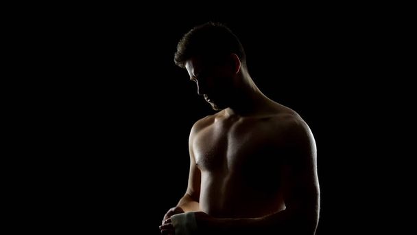 Boxer, který připravuje popruhy pro boj na tmavém pozadí, kickbox - Fotografie, Obrázek