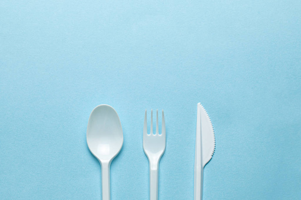 Plastic cutlery, forks, spoons and knives. Pollution of the environment with plastic and microplastics. Blue background. Copy space for text. - Photo, Image