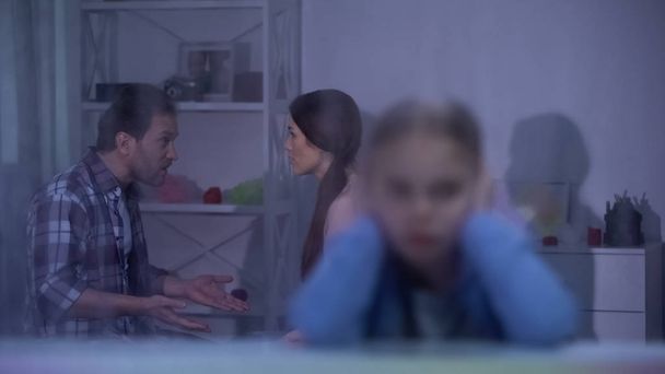 Parents arguing about child custody, girl closing ears on foreground, divorce - Фото, изображение