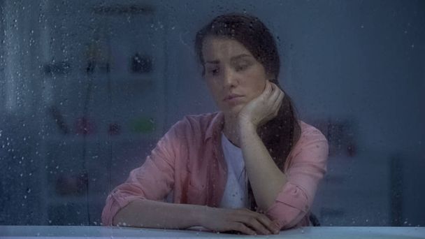 Pensive woman thinking about life problems, sitting behind rainy window, trouble - Foto, imagen
