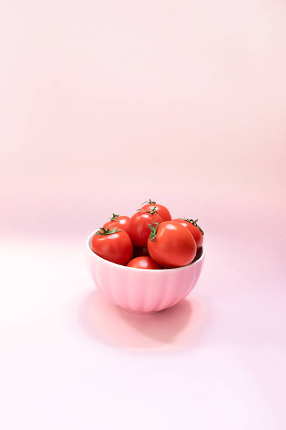 ピンクの背景に熟した赤いトマトとピンクのセラミックボウル。健康的な食事ビタミンバイオ食品 - 写真・画像