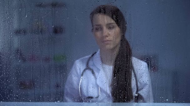 Female doctor with stethoscope depressed after patients death, rainy weather - Foto, afbeelding