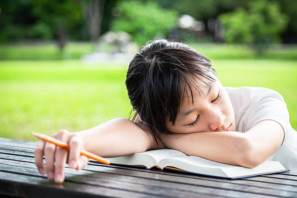 Asian little child girl sleeping falls asleep while reading book, female student sleep on table while doing her school homework in green nature,education,laziness and procrastination concept - Fotoğraf, Görsel