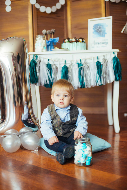 Χαριτωμένο μικρό αγόρι στα πρώτα του γενέθλια με μια σοκολάτα και πολύχρωμα μπαλόνια - Φωτογραφία, εικόνα