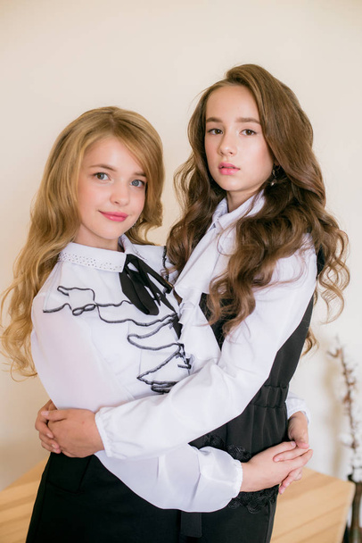 Δύο χαριτωμένα κορίτσια μαθήτριες με μακριά σγουρά μαλλιά σε μοντέρνα σχολικά ρούχα. Σχολική μόδα σε vintage ελίτ στυλ. - Φωτογραφία, εικόνα