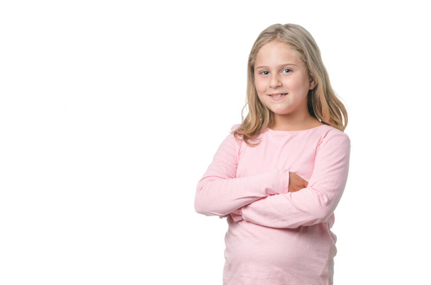 Petite fille blonde de huit ans souriante et les bras croisés sur fond blanc
 - Photo, image