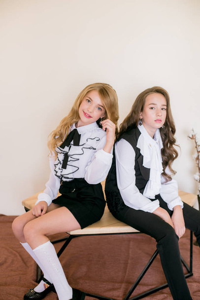 Two cute girls schoolgirls with long curly hair in fashionable school clothes. School fashion in vintage elite style. - Photo, image