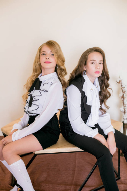 Two cute girls schoolgirls with long curly hair in fashionable school clothes. School fashion in vintage elite style. - Фото, изображение