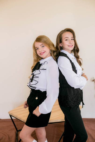 Two cute girls schoolgirls with long curly hair in fashionable school clothes. School fashion in vintage elite style. - 写真・画像