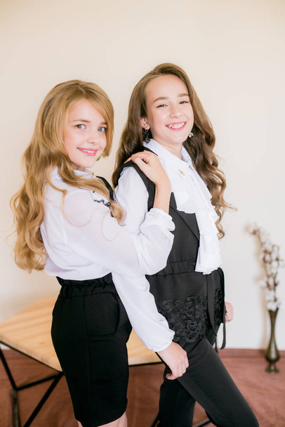 Two cute girls schoolgirls with long curly hair in fashionable school clothes. School fashion in vintage elite style. - Foto, Imagen
