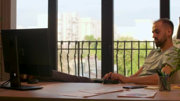 Бизнесмен в офисе стартап-компании печатает на ПК с ногами на столе
 - Кадры, видео