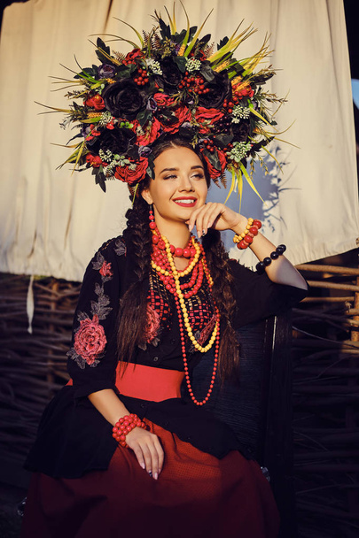 白いウクライナの本物の民族衣装と花輪のブルネットの女の子は、テラスに対してポーズをとっています。クローズ アップ. - 写真・画像
