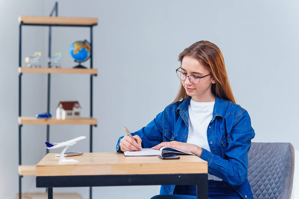 Beautiful young woman in office wearing denim clothes, make some notes on note book. - Foto, afbeelding