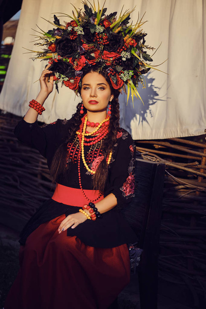 Brunetka dziewczyna w białym ukraińskim autentycznym Narodowym stroju i Wieniec kwiatów stwarza na taras. Zbliżenie. - Zdjęcie, obraz