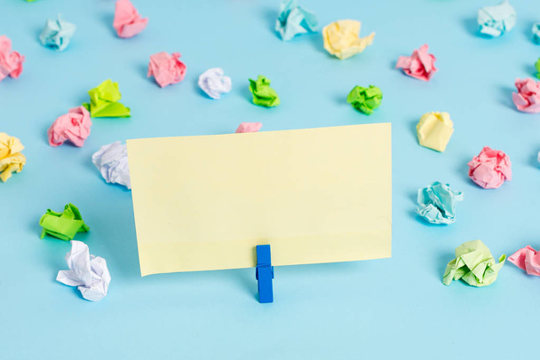 Colored crumpled sheets placed around the empty rectangle square shaped reminder note in the blue background. Office supplies, blank paper pinned by a fastener. - 写真・画像