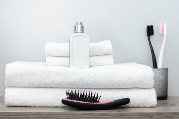 Clean folded towels, cream, comb and a pair of black and pink toothbrushes are on the shelf.  - Фото, изображение