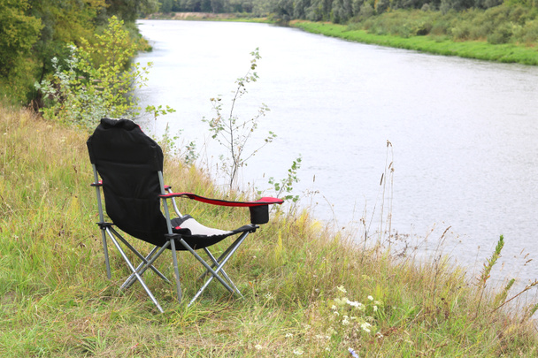 Portable folding tourist red armchair on green grass in summer on picnic near river - Fotó, kép