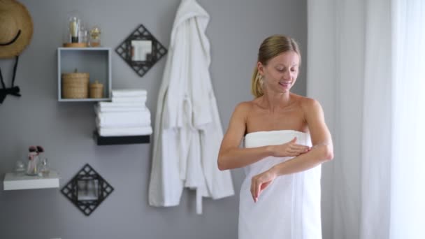 Body care. Beautiful woman wrapped in towel after shower is applying cream on her elbow - Materiaali, video