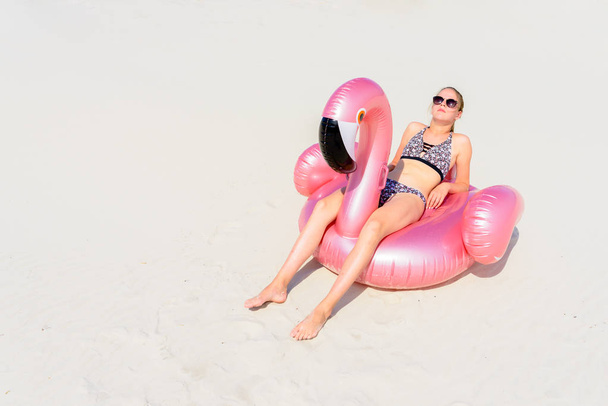砂浜のビーチでピンクのフラミンゴで日光浴をする若い女の子 - 写真・画像