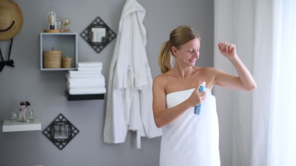 Body care. Beautiful woman wrapped in towel after shower is using antiperspirant. Girl is using deodorant spray for armpit skin - Materiaali, video