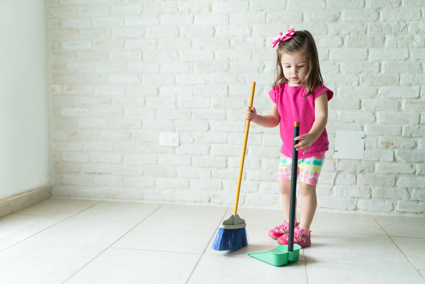 Full length of girl sweeping floor against wall in living room at home - Photo, Image