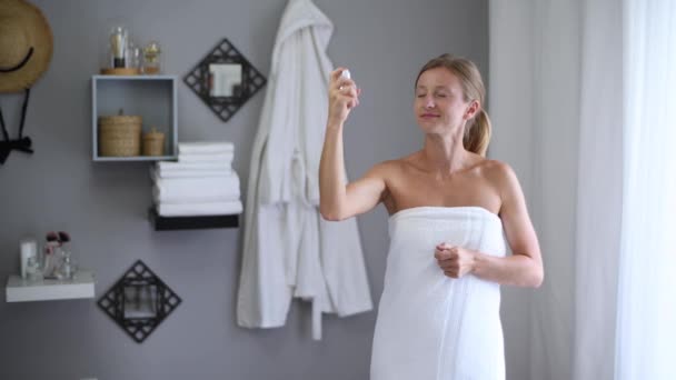 Hautpflege. schöne Frau in Handtuch gehüllt nach der Dusche trägt Parfüm auf ihrem Hals auf - Filmmaterial, Video