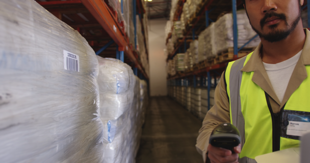 Close up of a young Asian male warehouse worker using barcode scanner and laptop computer to log goods stored in the warehouse, and shining scanner into camera.  - Footage, Video