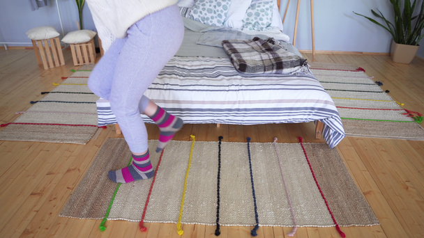 A woman in home clothes walks on a knitted bedside rug and correct her brown-pink sock. - Footage, Video