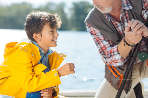 Bearded grandfather giving sea line to grandson while fishing together - 写真・画像