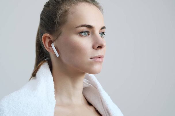 Sporty blonde girl with a white towel around her neck, in red sportswear and with white wireless headphones. - Foto, afbeelding