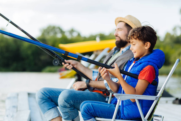 Father and son holding fishing tackles while fishing together - Foto, imagen
