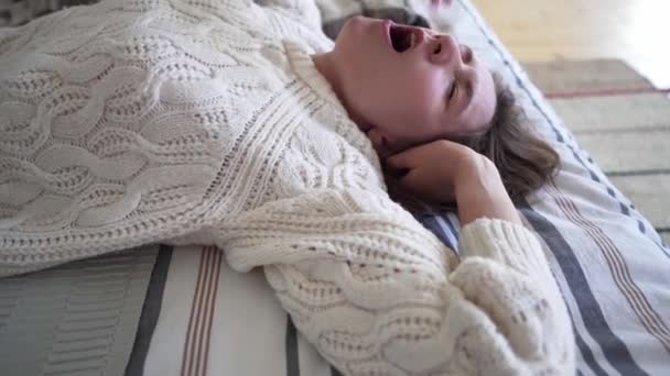 Rest time after a hard days work - Caucasian girl in a beautiful comfortable white sweater knitted from wool regains strength on the bed - Filmati, video