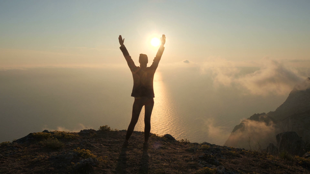 シルフエット若い女性の腕は、クリミアの高い山から海の上に美しい劇的な夕日を観察して伸びた. - 映像、動画
