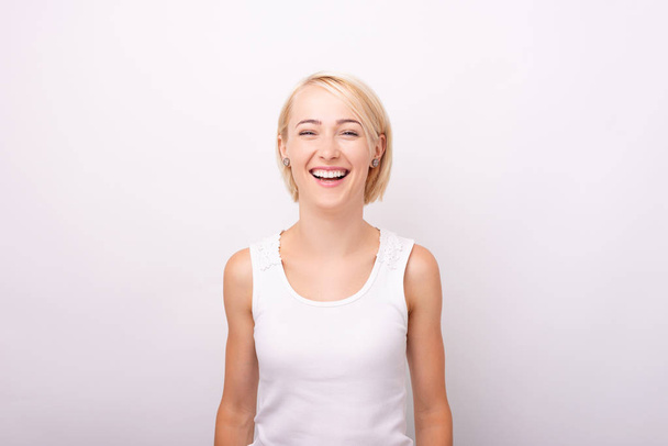 Портрет улыбающейся молодой женщины, стоящей на белом фоне
 - Фото, изображение