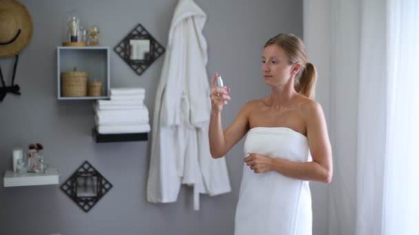 Skin care. Beautiful woman wrapped in towel after shower is spraying micellar water on face. - Πλάνα, βίντεο