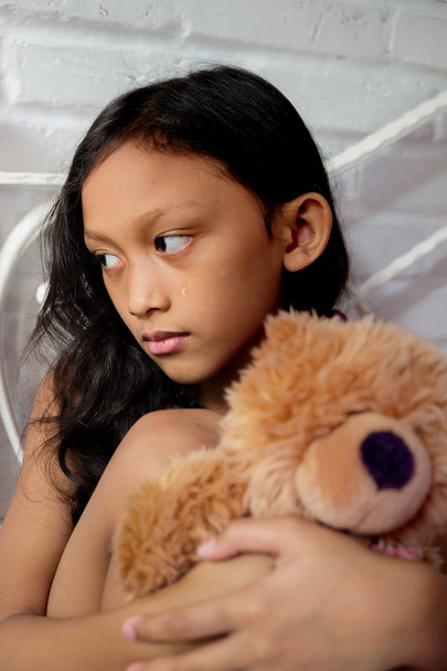 Muotokuva surullinen aasialainen pieni tyttö itkee halaus nallekarhu nukke
 - Valokuva, kuva